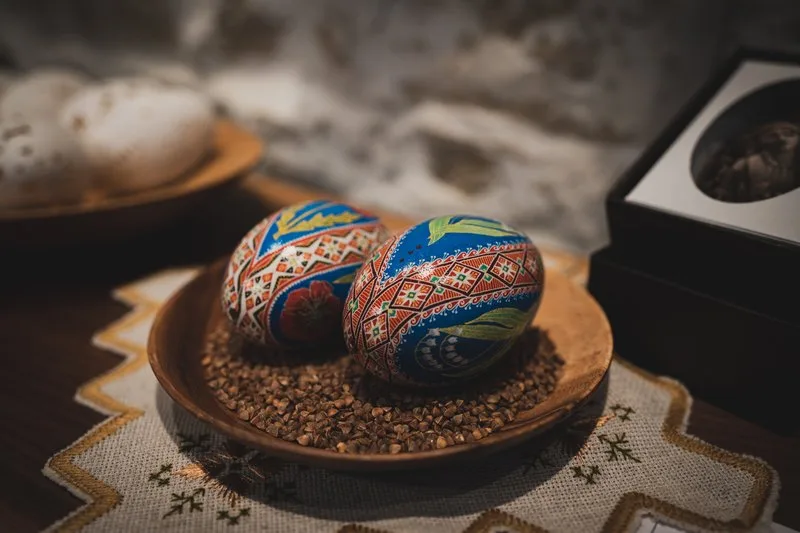 Deux Pissankas decorees sur un plat en bois avec des grains de sarrasin, sur un tissu brode